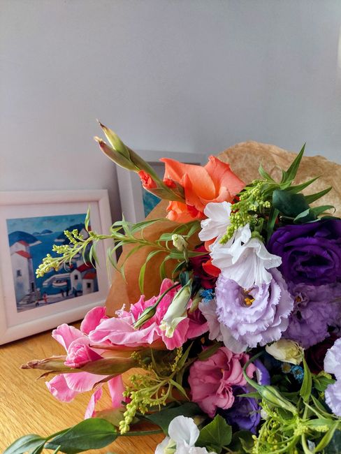 A vibrant floral arrangement featuring a mix of fresh flowers including purple lisianthus, white eustoma, pink snapdragons, orange gladiolus, and various green foliage, all arranged in a loose, natura